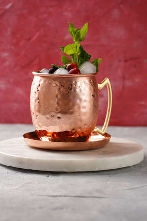 Traditional american alcoholic beverage moscow mule in copper mugs with cranberry and mint on white marble board - non-alcoholic cocktail versionの写真素材