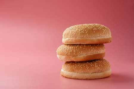 Three white wheat burger buns with sesame seeds on pink seamless surface, copy spaceの写真素材