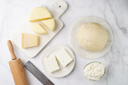 Various cheese types on marble and porcelain plates and fresh dough - ingredients for traditional georgian open pie khachapuriの写真素材