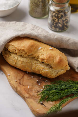 A loaf of homemade wheat bread on a wooden board on marble surfaceの写真素材