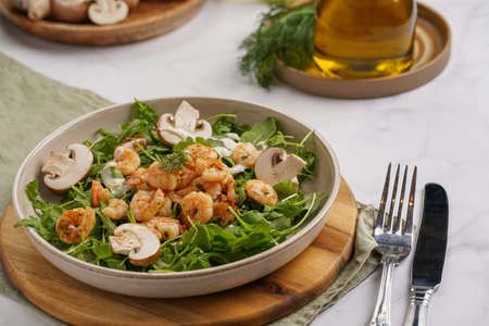 Arugula salad with shrimp and champignons, olive oil and dill on a wooden board on a white surfaceの写真素材
