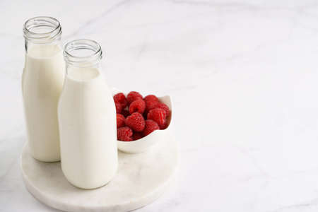 Two bottles with non-dairy milk and raspberries on round marble board