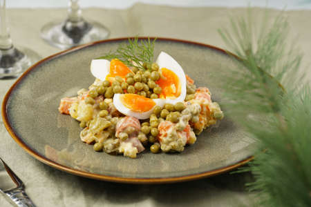 traditional east european dish for New Year's Eve - salad "Olivier" with potatoes, carrots, onion, peas, sausage eggs and mayonnaise on a green plateの写真素材