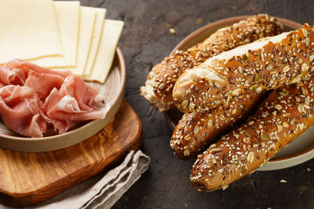 Savory breakfast ingredients: brown lye bread sticks garnished with oats, pork slices prosciutto,...