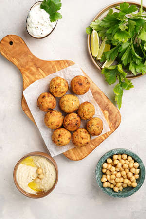 Traditional oriental chickpea deep fried falafel on a wooden board, tzatziki yoghurt sauce, hummus, fresh lime and green cilantro on light surface, top viewの写真素材