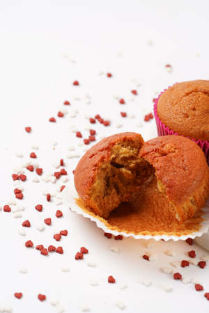 Several homemade white and pink muffins on marble board on white surface with heart-shaped red and white sugar decorationの写真素材