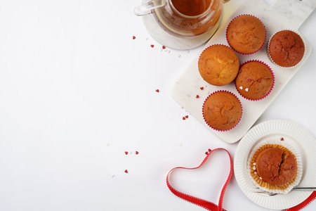 Several homemade white and pink muffins on marble board on white surface, red ribbon, heart-shaped red and white sugar decoration and tea-pot. copyspaceの写真素材