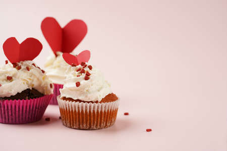 Three homemade white and chocolate muffins with white creamy frosting and heart-shared red and white...