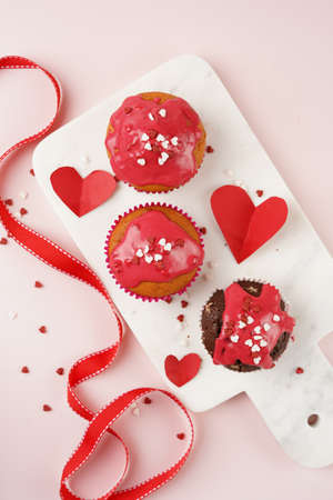 Three homemade white and chocolate muffins with red frosting and heart-shared red and white sugar...