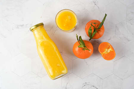 Tall glass with orange mango smoothie, several tangerines on white surface, top view flat layの写真素材
