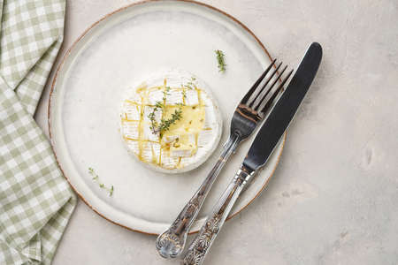 Oven baked camembert cheese on white plate, gray concrete surface. Homemade grilled brie with thyme, scandi style table settingの写真素材