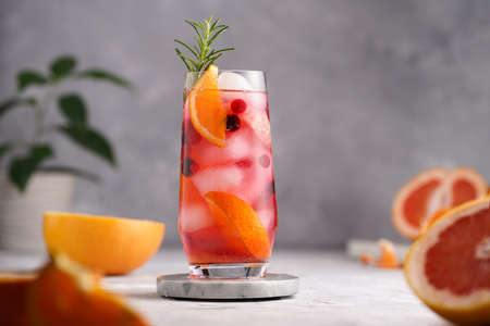 A tall glass with cold orange juice with grapefruit, frozen berries and ice cubes, rosemary, grapefruit half on gray backgroundの写真素材