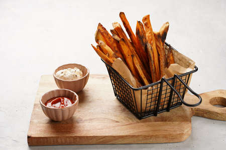 Healthy homemade oven baked sweet potato fries in a black deep frying basket net grid, wooden board,...
