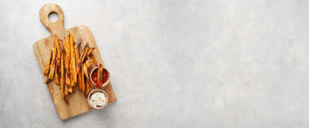 Healthy homemade oven baked sweet potato fries on a baking parchment, wooden board, with ketchup...