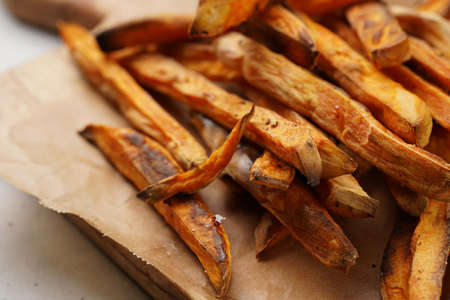 Healthy homemade oven baked sweet potato fries on a baking parchment, wooden board, with ketchup...