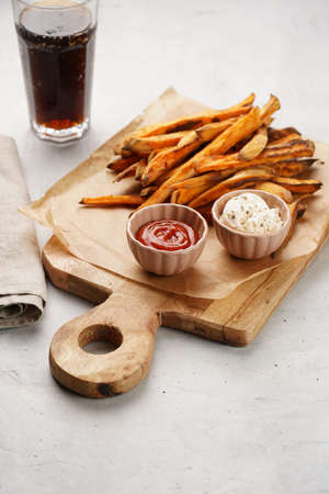 Healthy homemade oven baked sweet potato fries on a baking parchment, wooden board, with ketchup...