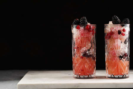 Two long glasses with non-alcoholic mocktail version of the classic blackberry and gin cocktail bramble on marble boardの写真素材
