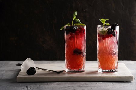 Two long glasses with non-alcoholic mocktail version of the classic blackberry and gin cocktail bramble on marble boardの写真素材