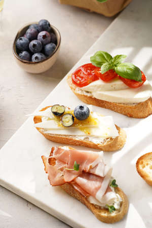 Italian antipasto bruschetta - white bread slices with smoked ham, goat cheese, blueberries,...