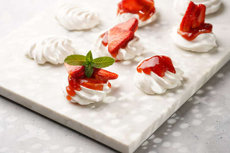 Mini-pavlova with fresh strawberries and red jam - delicious meringue cakes on marble board on...