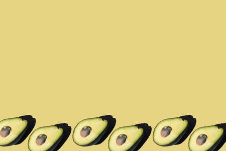 A half of an avocado with seed with hard light shadow on a pale green background: several avocados...