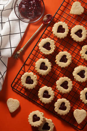 Round cookies with heart-shaped opening filled with red cherry jam on black baking rack, top view