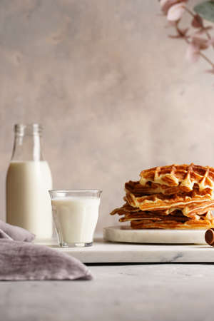 Sweet breakfast - fresh homemade belgian waffles with honey and powdered sugar stacked on white round marble board and small glass with milkの写真素材