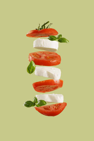 Italian salad caprese: slices tomato, mozzarella, basil leaves on green background flying in the air. Food levitationの写真素材