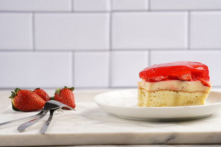 a piece of a three-layered cake with vanilla pudding, strawberry jelly and fresh strawberries on a white marble backgroundの写真素材