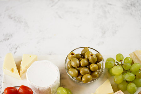 Cheese platter with organic cheeses - blue cheese cheddar, emmantal, french soft cheese with strong smell, italian parmesan, grapes, tomatoes, olives, nuts and crackers on marble board, copy spaceの写真素材