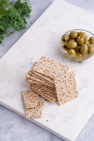 Healthy crunchy crisp crackers with sesame seeds and green olives on marble boardの写真素材