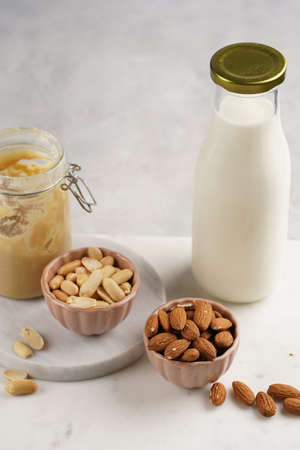 Peanuts, almonds in pink bowls, homemade peanut butter and almond milk on marble boards. Close up on nutsの写真素材