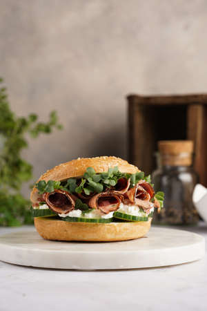 A bagel sandwich with pastrami, cucumber slices, watercress salad and ricotta on marble backgroundの写真素材