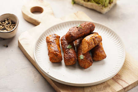 Traditional south european skinless sausages cevapcici made of ground meat and spices on white plate on light wooden board, with thyme and watercress saladの写真素材