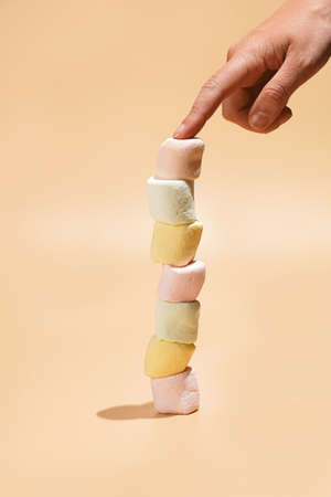 Several colorful marshmallows stacked on top of each other in balance and a female finger holding it...