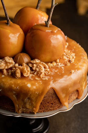 A brown cake with caramel coating and caramelized apples with tree branches on a black cake standの写真素材