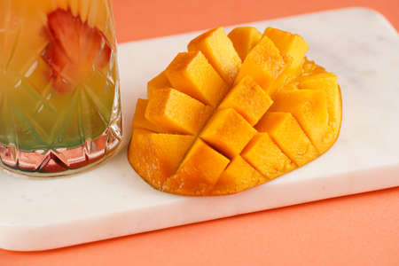 A mango fruit diced in cubes on marble board next to a glass with orange mocktail