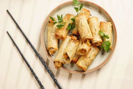 Traditional southeast asian starter dish spring or summer rolls - deep fried dim sum dumplings stuffed with vegetables with soy sauce, fresh coriander on gray plate with black chop sticks, top viewの写真素材