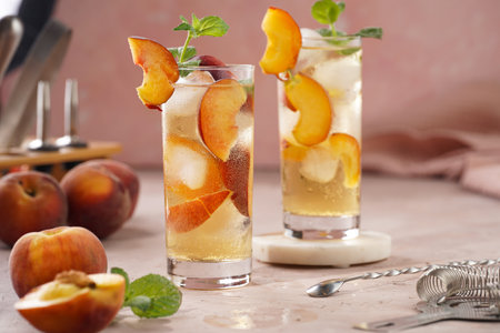 Two glasses with refreshing cocktail with ice cubes, peach slices and fresh mint on pale purple backgroundの写真素材