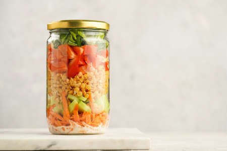 Trendy fresh detox summer salad layered in a glass mason jar: yoghurt dressing, carrots, cucumber,...