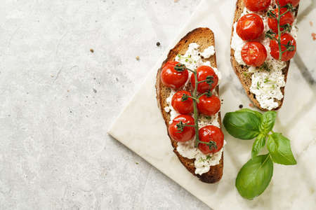 A sandwich with roasted cherry tomatoes with branch, fresh cottage cheese, green basil on a slice of...