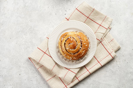 A round cinnamon pastry on a white plate on a linen checkered napkin on light pink grey, cup of coffee, jam, milk, top viewの写真素材