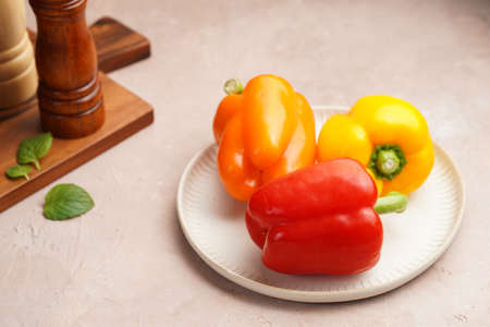 Three yellow, red and orange bell peppers on a white plate on a light pink kitchen surface