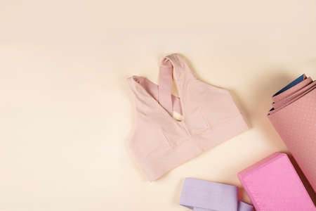 Clothes and equipment for a home workout or gym: pink and purple yoga blocks, yoga matt, training top on beige colored background, top view, space for textの写真素材