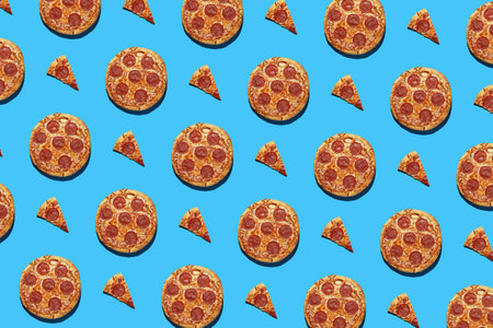 A hard light pattern of whole and cut salami pizza pieces on a seamless bright blue background, top...