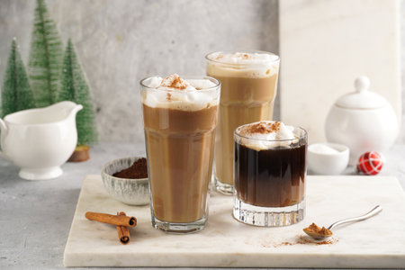 Three tall glasses with warm coffee drink with cinnamon, whipped milk foam and caramel on a marble...
