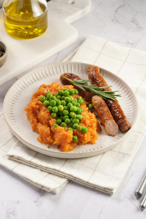 A lunch dish - boiled mashed sweet potato, steamed green peas and pork roasted sausages in a light gray bowl on a marble backgroundの写真素材