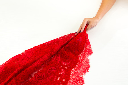 Woman's hand pulls a red fabric with lace on white table, backgroundの写真素材