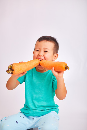 Baby boy in a turquoise shirt, eating huge carrots - fruits and healthy foodの写真素材