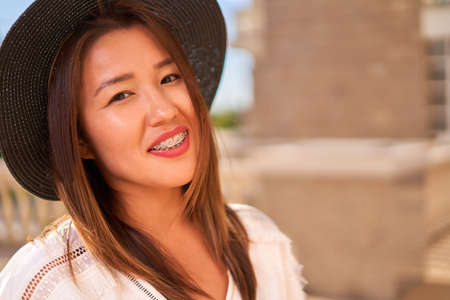 Proud smile of a girl not embarrassed by braces, a girl of Asian appearance in a hat and white T-shirt. High quality photoの写真素材
